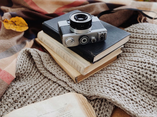 camera op stapel boeken buiten op een gehaakt wollen kleed in de herfstbladeren